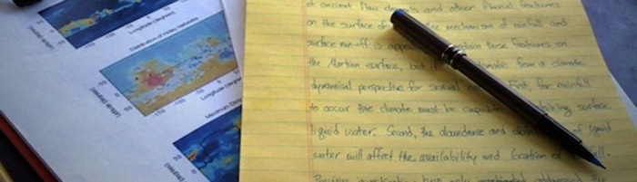 Image of papers, one with plots on it and one with handwritten sentences. All of it representing the paper writing process.